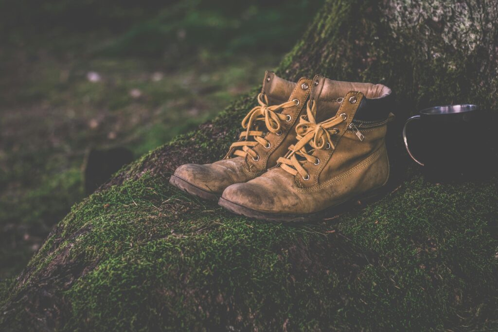 Brown leather hiking boots and cup on a moss-covered forest background, evoking adventure.